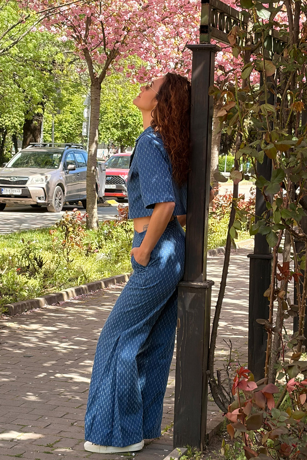 Person in blue outfit leaning against a pole with cherry blossoms in the background