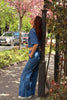 Person in blue outfit leaning against a pole with cherry blossoms in the background